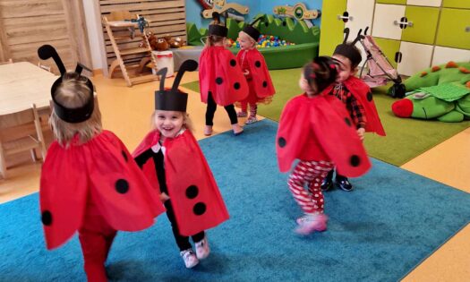 Dzieci przebrane za biedronki tańczą w parach na turkusowym dywanie. W tle widać salę zabaw.