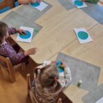 Dzieci siedzą na krzesełkach przy stoliku i wyklejają planetę Ziemię z papieru.