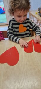 Chłopiec siedzi przy stole i łączy w pary papierowe czerwone serduszka.