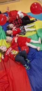 Dzieci leżą z czerwonymi balonikami na kolorowej chuście.