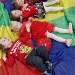 Dzieci leżą z czerwonymi balonikami na kolorowej chuście.