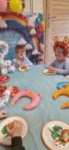 Dzieci siedzą przy stole urodzinowym i częstują się babeczkami.