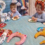 Dzieci siedzą przy stole urodzinowym i częstują się babeczkami.