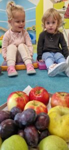 Dzieci siedzą na podusiach i oglądają owoce.