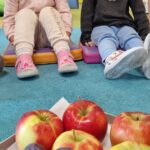 Dzieci siedzą na podusiach i oglądają owoce.