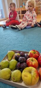 Dzieci siedzą na podusiach i oglądają owoce z sadu.