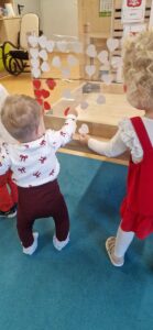 Dzieci stoją i naklejają czerwone i białe serduszka na przyklejonej taśmie, tworząc flagę biało- czerwoną.