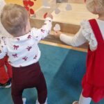 Dzieci stoją i naklejają czerwone i białe serduszka na przyklejonej taśmie, tworząc flagę biało- czerwoną.