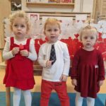 Dzieci stoją koło siebie ubrane na biało- czerwono. W tle widać flagę biało- czerwoną