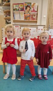 Dzieci stoją koło siebie ubrane na biało- czerwono. W tle widać flagę biało- czerwoną