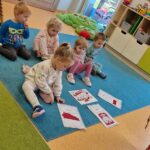 Dzieci siedzą na turkusowym dywanie i oglądają wydrukowane symbole narodowe.