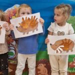 Dzieci stoją przy dekoracjach jesiennych i trzymają w dłoni pracę plastyczną "jeżyk"