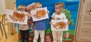 Dzieci stoją przy dekoracjach jesiennych i trzymają w dłoni pracę plastyczną "jeżyk"